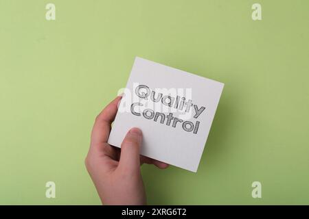Une main tenant un morceau de papier avec le mot contrôle qualité écrit dessus. L'image transmet l'importance de maintenir des normes élevées et ensuri Banque D'Images
