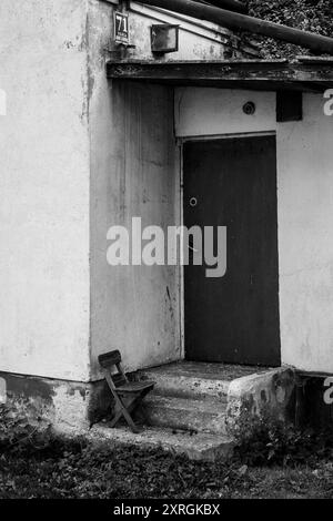 Chaise en bois d'enfant oublié devant une maison abandonnée à Opoczno, Pologne. Pauvreté, post-communisme, délabrement, oublié. Image noir et blanc Banque D'Images