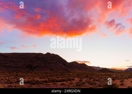 Superbe coucher de soleil illuminant les montagnes et les terrains désertiques. Des teintes brillantes d'orange, de rose et de violet peignent le ciel, créant une atmosphère sereine en t Banque D'Images