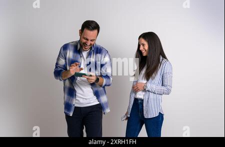 Souriant jeune petite amie regardant joueur petit ami jouant au jeu vidéo sur téléphone intelligent. Couple joyeux habillé en décontractés avec des téléphones portables debout A. Banque D'Images