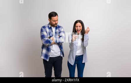 Petit ami sérieux avec les bras croisés regardant furieusement la petite amie extatique criant dans le succès tout en jouant au jeu vidéo. Jeune homme regardant la femme Banque D'Images