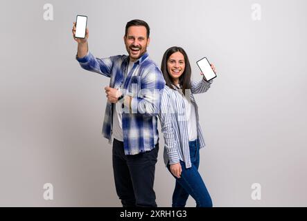 Joyeux jeune homme et femme montrant l'écran blanc des téléphones intelligents et la promotion des applications de commerce électronique. Couple joyeux habillé dans la publicité occasionnelle sur cel Banque D'Images