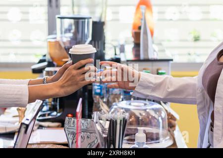 Un beau barista asiatique qui donne une tasse de café aux clients qui attendent les commandes au comptoir du café avant de discuter et de saluer les clients b. Banque D'Images