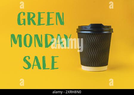 Une tasse avec un couvercle vert est sur fond jaune avec les mots Green Monday Sale écrits en dessous Banque D'Images