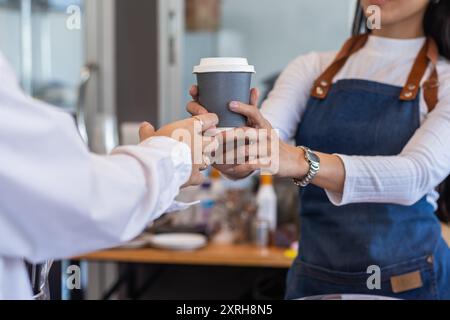 Un beau barista asiatique qui donne une tasse de café aux clients qui attendent les commandes au comptoir du café avant de discuter et de saluer les clients b. Banque D'Images