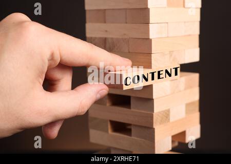 Homme enlevant le bloc de bois avec le contenu de la tour sur fond sombre, gros plan Banque D'Images