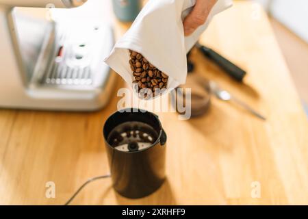 Gros plan de grains de café versés dans un moulin avec une machine à café en arrière-plan. Banque D'Images