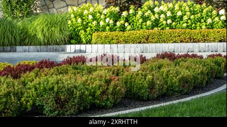 Un jardin vibrant présente une herbe verte luxuriante, des arbustes colorés et des parterres de fleurs en fleurs dans un paysage bien entretenu. Banque D'Images