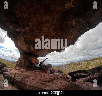 Homme pointant vers les étoiles et les constellations peintes sur le plafond de l'ancien abri aborigène dans la roche, la section des remparts, le parc national de Chillagoe, l'outback que Banque D'Images