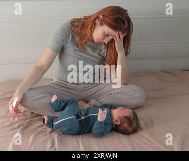 Une femme caucasienne est assise sur un lit à côté d'un bébé qui pleure. Dépression du post-partum. Banque D'Images