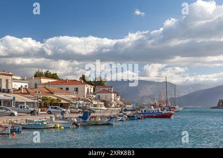 Vue panoramique sur le front de mer de Galaxidi avec l'architecture grecque traditionnelle, bateaux de pêche amarrés, et toile de fond de montagne sous un ciel lumineux à Fokida Banque D'Images