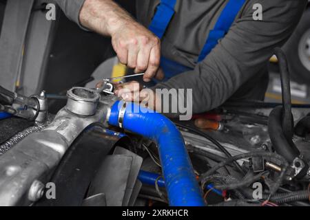 Un mécanicien ajuste méticuleusement les composants du moteur à l'aide d'une clé dans un garage bien équipé. L'accent est mis sur les détails complexes des machines et les mains habiles au travail, illustrant un moment d'entretien automobile. Banque D'Images