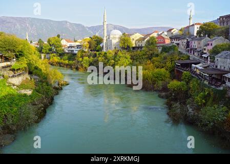 Vieille ville de Mostar et Neretva : vue depuis le vieux pont de la rivière et ses rives verdoyantes avec la rue Kujundziluk et la mosquée Koski Mehmed Pacha Banque D'Images