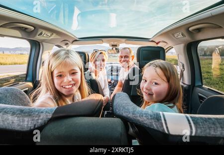 Jeune couple avec filles portrait assis dans une voiture moderne avec un toit transparent. Moments heureux en famille, enfance, restauration rapide ou voyage en auto Banque D'Images