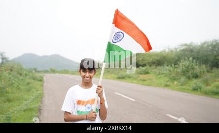 Étudiant indien ou enfants tenant ou agitant tricolore avec de la verdure en arrière-plan, célébrant l'indépendance ou le jour de la République. Har Ghar Tiranga Banque D'Images