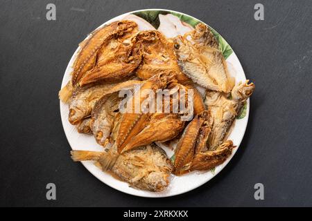 Ikan masin goreng ou poisson salé frit dans une plaque blanche, isolé sur fond noir. Cuisine traditionnelle malaisienne et indonésienne. Banque D'Images