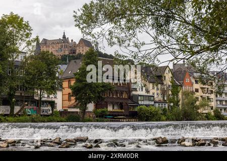 Marburg, Allemagne. 09 août 2024. Le château de Marburg, également connu sous le nom de Landgrave's Castle Marburg, s'élève au-dessus de la ville. Vue depuis les rives du Lahn sur les maisons du quartier sud jusqu'à la colline du château. Il est né comme un château au XIe siècle et a été converti en palais résidentiel par les Landgraves de Hesse au XIIIe siècle. Depuis 1981, le château abrite le musée d'histoire de l'art de l'Université Philipps de Marbourg. Crédit : Christian Lademann/dpa/Alamy Live News Banque D'Images