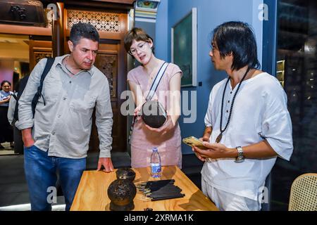 (240811) -- HAIKOU, 11 août 2024 (Xinhua) -- Wu Mingju (R) présente des œuvres de sculpture de coquilles de noix de coco à des clients étrangers dans la vieille rue Qilou à Haikou, dans la province de Hainan, au sud de la Chine, le 22 avril 2024. La sculpture de coquille de noix de coco, une forme d'art qui implique la création de dessins à l'aide d'outils de sculpture sur la coquille dure d'une noix de coco, a été répertoriée comme l'un des patrimoines culturels immatériels nationaux en 2008. Wu Mingju, un héritier de la sculpture de coquille de noix de coco, s'est engagé à l'héritage et à la promotion de cet art ancien et complexe depuis 33 ans en explorant l'innovation technique, en mettant en place co Banque D'Images