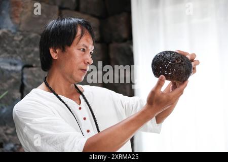 (240811) -- HAIKOU, 11 août 2024 (Xinhua) -- Wu Mingju vérifie son œuvre de sculpture de coquille de noix de coco dans un atelier à Haikou, dans la province de Hainan, dans le sud de la Chine, le 9 août 2024. La sculpture de coquille de noix de coco, une forme d'art qui implique la création de dessins à l'aide d'outils de sculpture sur la coquille dure d'une noix de coco, a été répertoriée comme l'un des patrimoines culturels immatériels nationaux en 2008. Wu Mingju, un héritier de la sculpture de coquille de noix de coco, s'est engagé à l'héritage et à la promotion de cet art ancien et complexe depuis 33 ans en explorant l'innovation technique, en mettant en place des cours de sculpture de coquille de noix de coco dans les écoles Banque D'Images