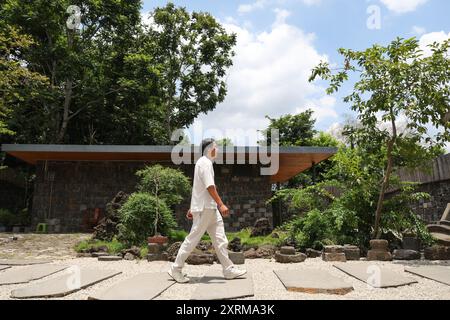 (240811) -- HAIKOU, 11 août 2024 (Xinhua) -- Wu Mingju marche dans une cour dans un atelier à Haikou, dans la province de Hainan, dans le sud de la Chine, le 9 août 2024. La sculpture de coquille de noix de coco, une forme d'art qui implique la création de dessins à l'aide d'outils de sculpture sur la coquille dure d'une noix de coco, a été répertoriée comme l'un des patrimoines culturels immatériels nationaux en 2008. Wu Mingju, un héritier de la sculpture de coquille de noix de coco, s'est engagé à l'héritage et à la promotion de cet art ancien et complexe depuis 33 ans en explorant l'innovation technique, en mettant en place des cours de sculpture de coquille de noix de coco dans les écoles et en cultivant les jeunes Ar Banque D'Images