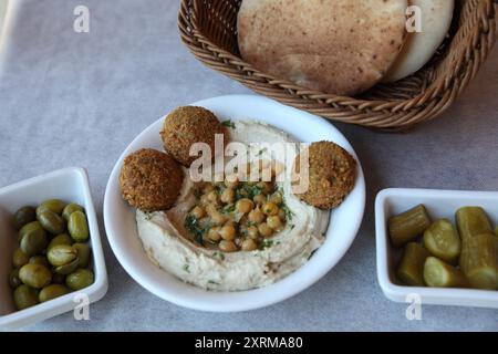 Houmous, plat du moyen-Orient à base de purée de pois chiches cuites mélangées à du tahini, du jus de citron et de l'ail, du pita, des boules de falafel, des concombres marinés et des olives Banque D'Images