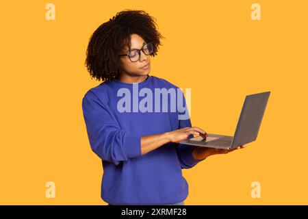 Jeune homme engagé avec ordinateur portable sur fond jaune vif Banque D'Images