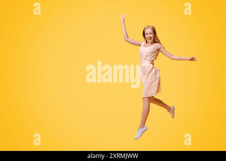 Jeunesse insouciante. Fille jouante en forme de Teen qui saute dans l'air sur fond jaune Banque D'Images