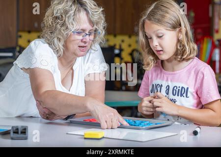 Un enseignant aide une jeune fille avec une orthographe. Le professeur pointe vers une lettre, et la fille la regarde attentivement. Banque D'Images