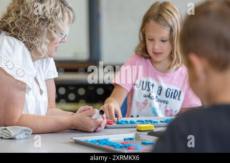 Un enseignant aide une jeune fille avec une orthographe. Le professeur pointe vers une lettre, et la fille la regarde attentivement. Banque D'Images