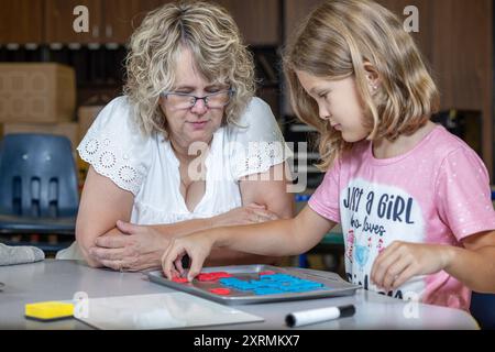 Un enseignant aide une jeune fille avec une orthographe. Le professeur pointe vers une lettre, et la fille la regarde attentivement. Banque D'Images