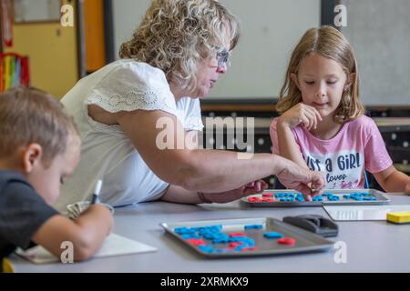 Un enseignant aide une jeune fille avec une orthographe. Le professeur pointe vers une lettre, et la fille la regarde attentivement. Banque D'Images