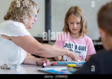 Un enseignant aide une jeune fille avec une orthographe. Le professeur pointe vers une lettre, et la fille la regarde attentivement. Banque D'Images