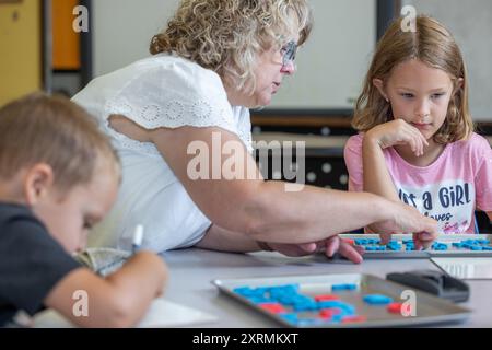 Un enseignant aide une jeune fille avec une orthographe. Le professeur pointe vers une lettre, et la fille la regarde attentivement. Banque D'Images