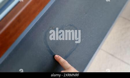 Coeur fait de poussière sur le rebord de la fenêtre. Le doigt d'une femme dessine un cœur sur la fenêtre, l'amour. Banque D'Images