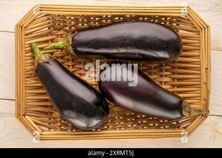 Trois aubergines mûres dans un panier sur une table en bois, macro, vue de dessus. Banque D'Images