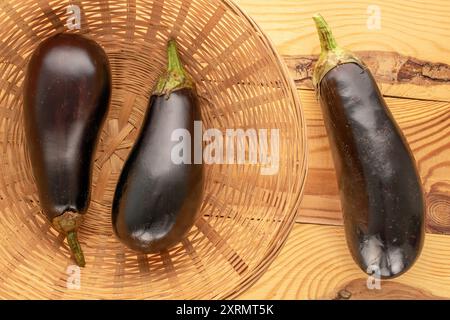 Trois aubergines mûres dans un panier sur une table en bois, macro, vue de dessus. Banque D'Images