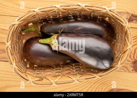 Trois aubergines mûres dans un panier sur une table en bois, macro, vue de dessus. Banque D'Images