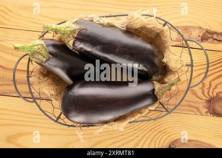 Trois aubergines mûres dans un panier sur une table en bois, macro, vue de dessus. Banque D'Images