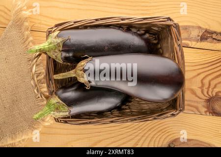 Trois aubergines mûres dans un panier sur une table en bois, macro, vue de dessus. Banque D'Images