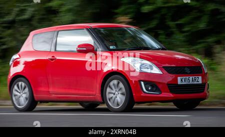 Potterspury, Northants, UK - 11 août 2024 : 2015 voiture Suzuki Swift rouge voyageant sur une route britannique Banque D'Images