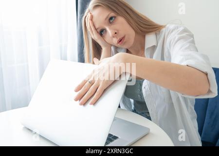Femme d'affaires épuisée fermant l'ordinateur portable tout en travaillant à la maison se sentant stressée, frustrée, ennuyée et fatiguée. Femmes avec les défis du travail à distance Banque D'Images