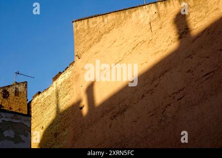 Les murs de vieux bâtiments créent des ombres intéressantes, tandis qu'une antenne de télévision se tient en évidence au sommet de la structure en plein soleil. Banque D'Images