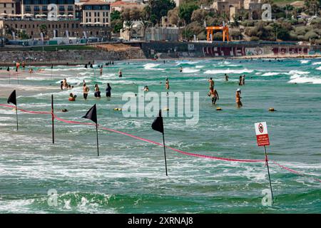 Plage Charles clore avec drapeaux noirs à tel Aviv. Les gens nagent malgré les grosses vagues Banque D'Images