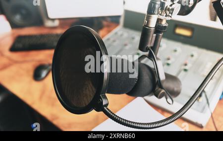 Microphone de studio d'enregistrement professionnel avec filtre pop, prêt pour l'enregistrement de podcast ou vocal. Équipement de production audio de haute qualité sur un bureau en bois, arrière-plan flou du mixeur sonore. Banque D'Images