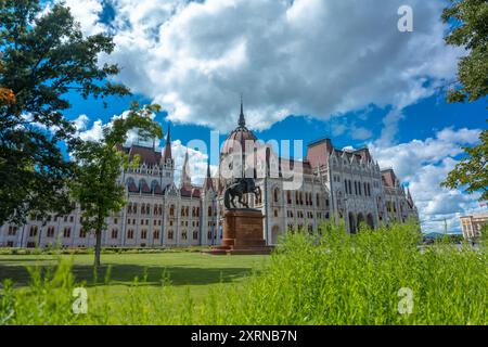 Budapest, Hongrie - 16 juin 2024 : bâtiment du Parlement à la chaude journée. Statue équestre Rakoczi Ferenc au premier plan. Journée ensoleillée, ciel nuageux moyen. Banque D'Images