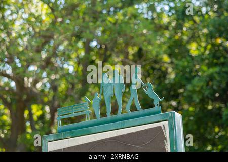 Éléments décoratifs en acier avec des silhouettes de personnes dans un parc. Famille avec un enfant, propriétaire de chien avec animal de compagnie, oiseau sur un banc. Beau bokeh en arrière-plan Banque D'Images