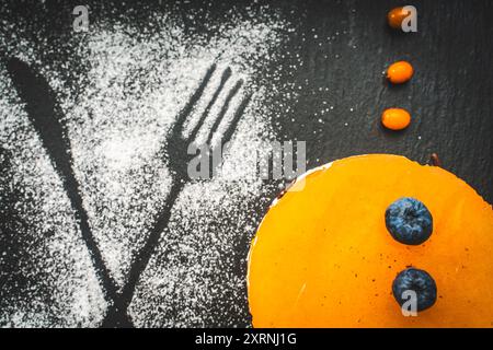 Dessert en couches : gelée d'argousier ou de mangue, crème au fromage cottage, gâteau éponge au chocolat. Gâteau sur un panneau de mica noir sur un fond noir. Beauti Banque D'Images