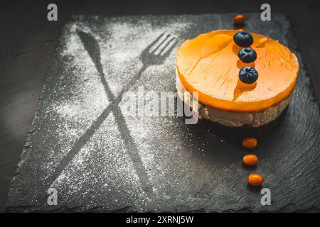 Dessert en couches : gelée d'argousier ou de mangue, crème au fromage cottage, gâteau éponge au chocolat. Gâteau sur un panneau de mica noir sur un fond noir. Beauti Banque D'Images