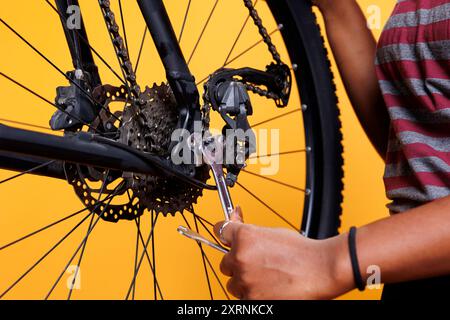 Image détaillée montrant une paire de mains faisant l'entretien en fixant habilement la roue de vélo avec l'outil de travail essentiel. Gros plan d'une clé de serrage femme noire pour serrer les pièces de bicyclette. Banque D'Images