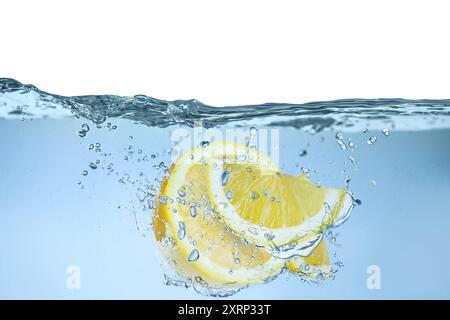 Citrons frais tombant dans l'eau sur fond blanc Banque D'Images